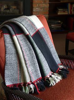 a chair with a blanket on it in front of a fire place and bookshelf