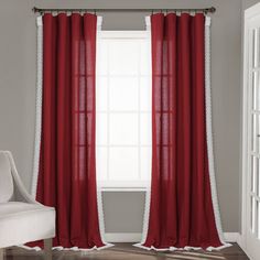 a white chair sitting in front of a window covered in red curtain panels and lace trim