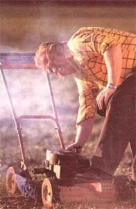 a man bending over to pick up something off the ground with a lawn mower