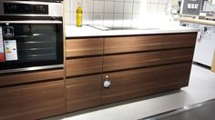 an oven and counter in a kitchen with white tile backsplashes, wood grain cabinetry, and stainless steel appliances