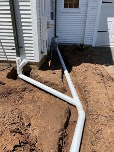 a white pipe laying on top of dirt next to a house