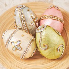 three decorated eggs sitting on top of a wooden plate with gold trimmings and crystals