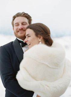 a bride and groom smile as they stand in the snow