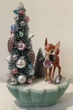 a small deer figurine standing next to a christmas tree with ornaments on it