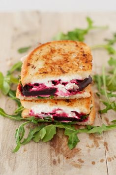 two grilled cheese sandwiches with berry filling on a wooden table next to fresh green leaves