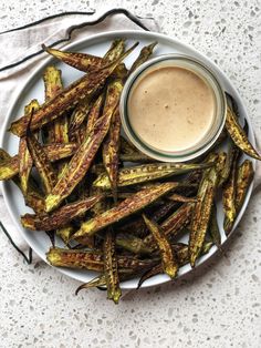 a white plate topped with fried asparagus next to a cup of dipping sauce