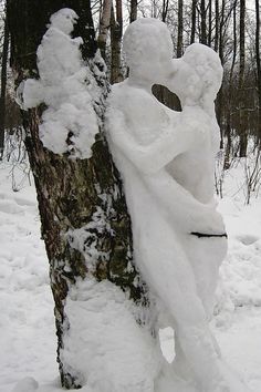 a snow covered statue sitting on top of a tree in the middle of a forest