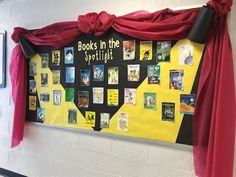 a bulletin board with books in the spotlight and red drapes hanging from it's sides