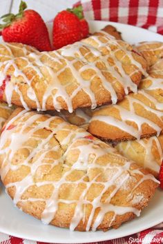 strawberry shortcakes with icing and strawberries on a white plate next to a red checkered tablecloth