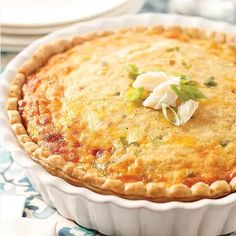 a quiche with cheese on top in a white dish sitting on a blue and white table cloth