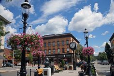 a clock on a pole in the middle of a street with flowers and benches around it