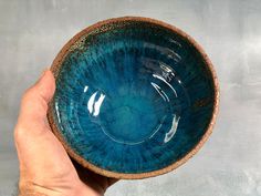 a hand is holding a blue bowl in front of a gray wall and concrete background