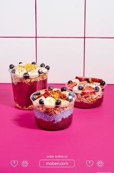 three desserts with blueberries, strawberries and granola in them on a pink surface