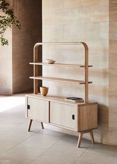 a wooden shelf sitting next to a plant on top of a white tiled floor in front of a wall