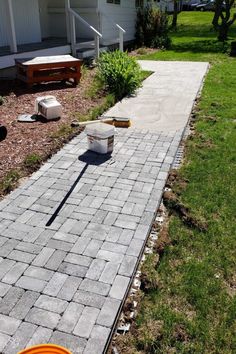 a brick walkway in front of a house with a bucket and shovel on the side