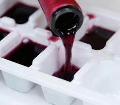 someone pouring red liquid into an ice cube tray with black and white containers in it