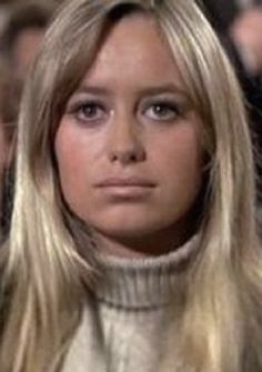 a woman with long blonde hair wearing a turtle neck sweater and looking at the camera