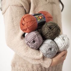 a woman holding several balls of yarn in her hands and wearing a sweater with an orange tag on it