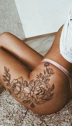 a woman laying on the floor with her stomach covered in flowers and leaves tattoo design