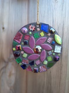 a colorful glass ornament hanging on a wooden wall next to a wood fence