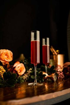 two wine glasses filled with liquid sitting on top of a wooden table next to flowers