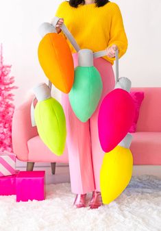 a woman standing in front of a pink couch with colorful decorations on it and holding a pair of scissors