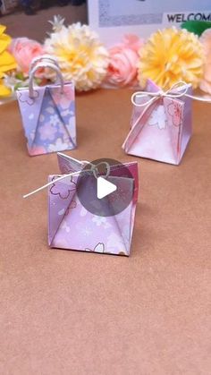 three small pink and purple boxes with bows on them sitting on a table next to flowers