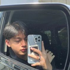 a young man taking a selfie in his car mirror with his cell phone up to his face