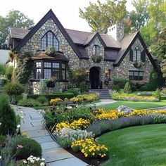 a stone house with lots of flowers in the front yard and walkway leading to it