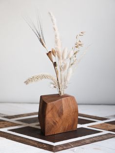 a wooden vase with dried plants in it on a checkered tile flooring area