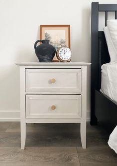 a white nightstand with two drawers and a clock on top