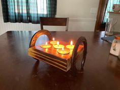 a wooden tray with four lit candles in it sitting on a table next to a window