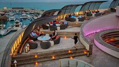 people are sitting at tables on the roof of a boat dock with boats in the water