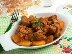 a white bowl filled with meat and potatoes on top of a green checkered table cloth