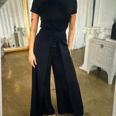 a woman standing in front of a mirror wearing a black top and wide legged pants