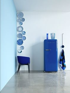 a blue refrigerator sitting in the corner of a room with plates hanging on the wall