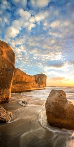 the sun is setting over some rocks in the water at the beach with waves coming up on them