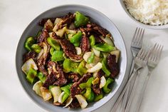 a bowl filled with meat and veggies next to a plate of rice on a table