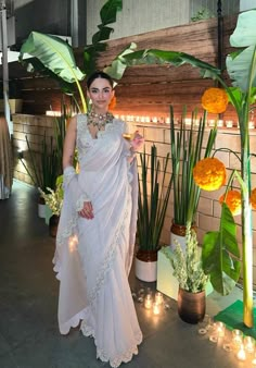 a woman in a white sari standing next to plants