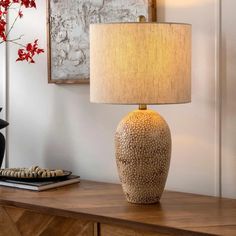 a table lamp sitting on top of a wooden dresser next to a vase with red flowers