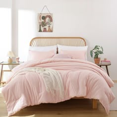 a bed with pink comforter and pillows in a white room next to a wooden headboard