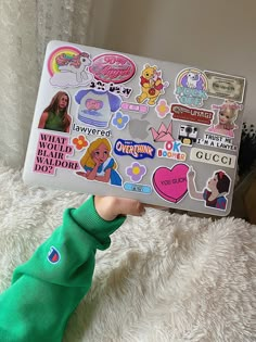 a person holding up a laptop with stickers on it