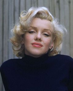 a woman with blonde hair wearing a black shirt and posing for a photo in front of a fence