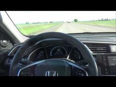 the inside view of a car driving on a road with grass and trees in the background