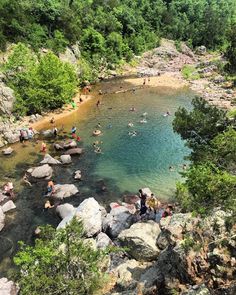 many people are swimming in the water near some rocks