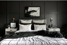 a bedroom with black walls and white bedding, two nightstands and a painting on the wall