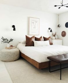 a white bed with brown pillows in a bedroom next to a plant on the wall