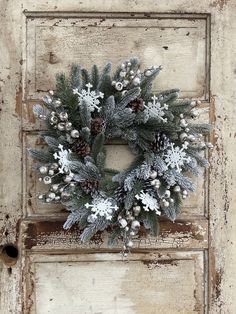 a wreath is hanging on an old door with snowflakes and pine cones around it