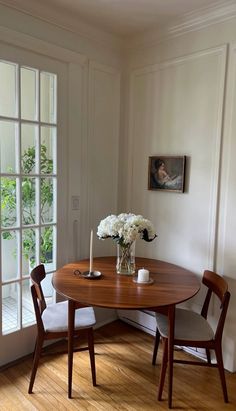 a dining room table with two chairs and a vase filled with flowers on top of it