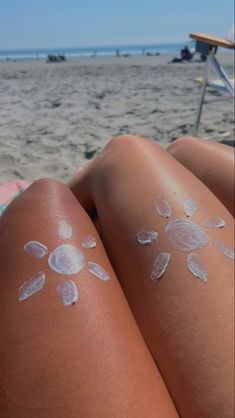 a woman laying on top of a sandy beach next to the ocean covered in sunscreens